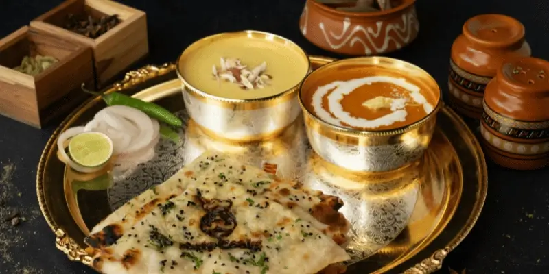 A plate with stuffed flatbreads served with a pat of butter and small bowls of yogurt, pickle, and chutney.
