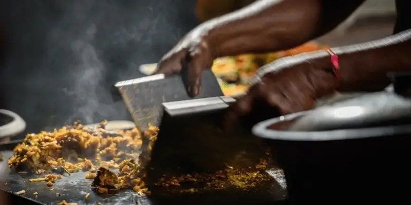 Hands cooking mixed vegetables on a hot grill with steam rising.