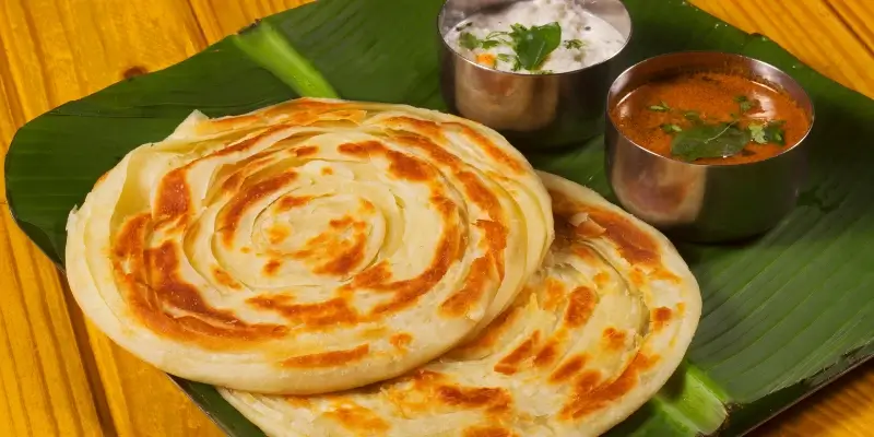 Crispy layered parotta served on a banana leaf with coconut chutney and curry in small metal bowls