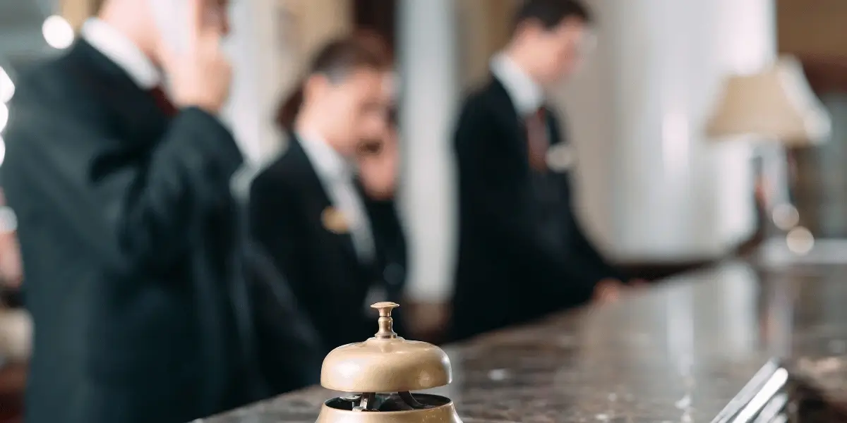 Two hotel reception staff standing at the front desk, one speaking on the phone and the other holding a clipboard.