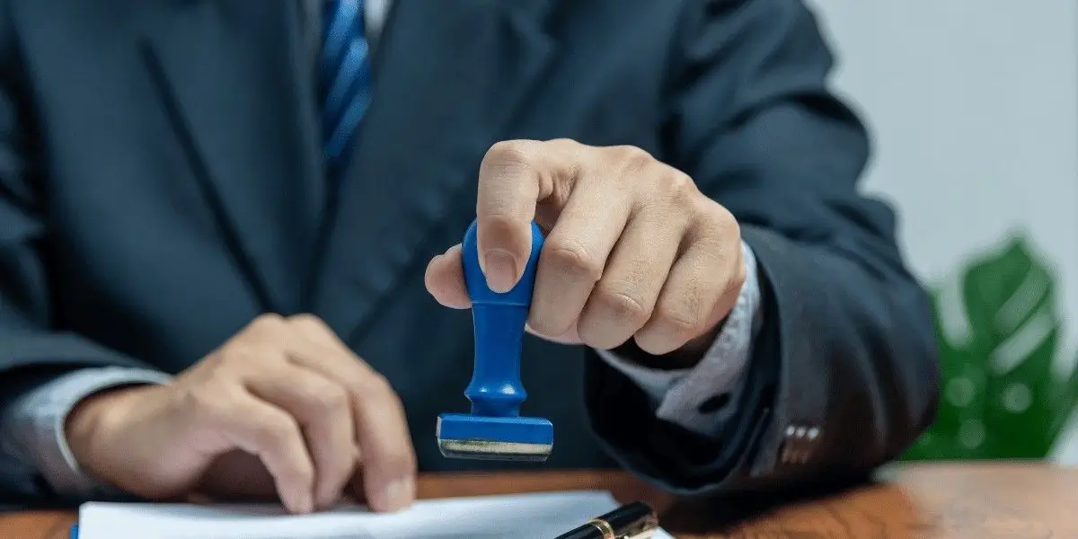 Person in a suit pressing a blue stamp onto paperwork