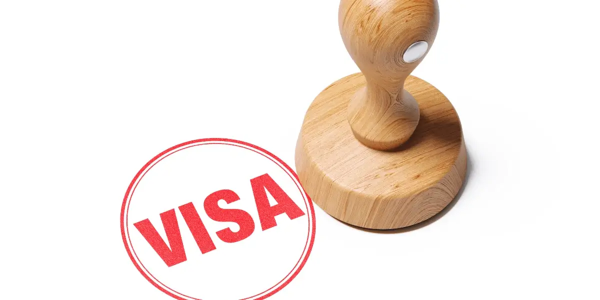 A wooden stamp sits on a white surface next to a bright red circular mark with the word VISA in bold red letters.